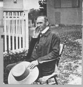 SA0136 - A photograph of an unidentified man, most likely Frederick Evans, outside and with a wagon shed and garden shed behind him. He is holding a large brimmed hat.